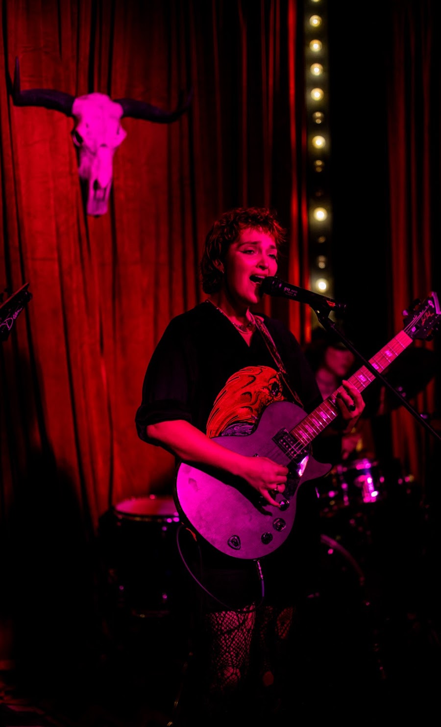 Singer-songwriter performing with guitar under red and purple stage lights